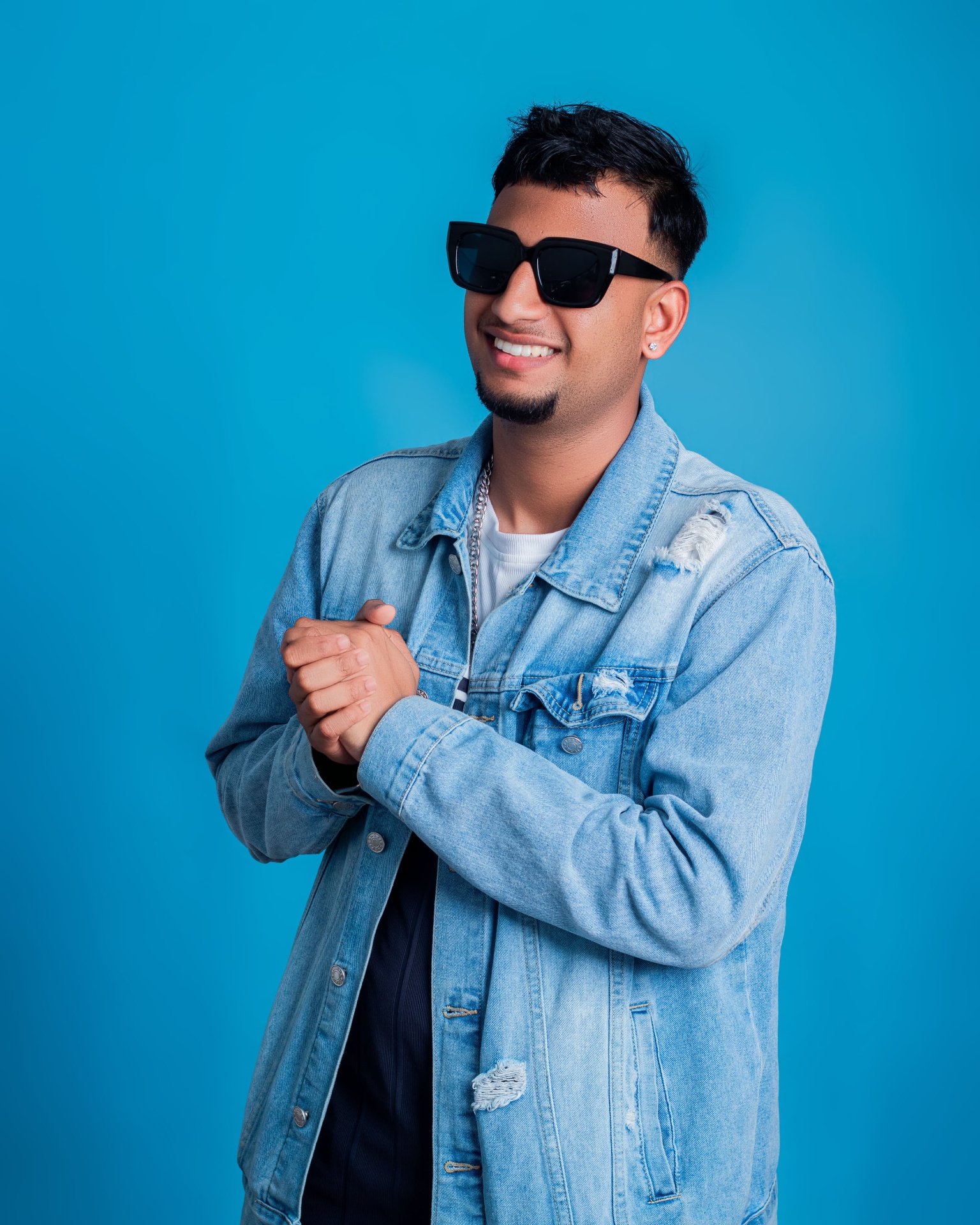 Man in a denim jacket and sunglasses against a blue backdrop