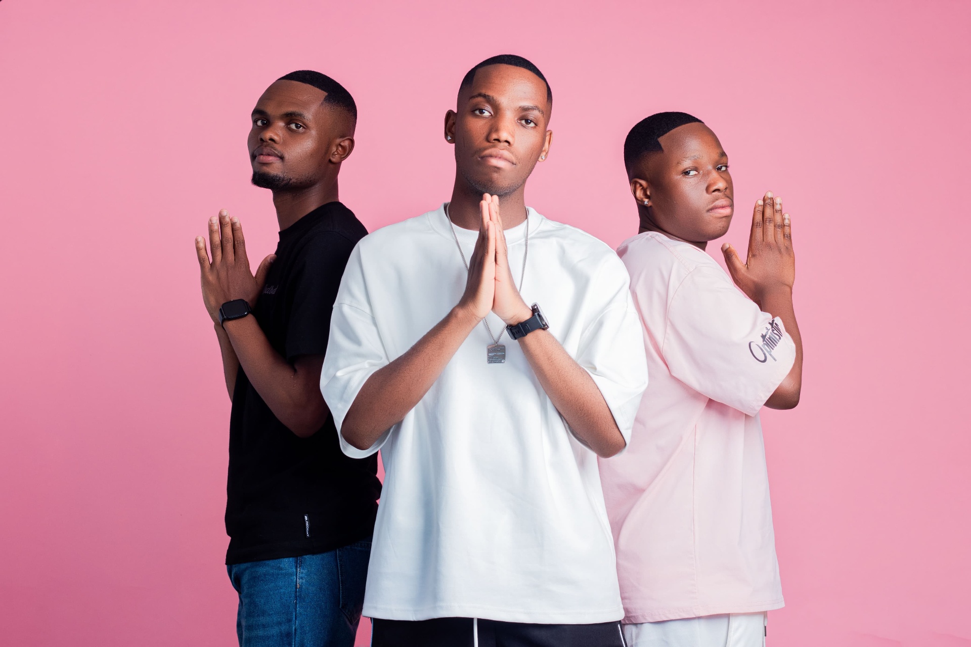 Three men posing together against a pink studio backdrop