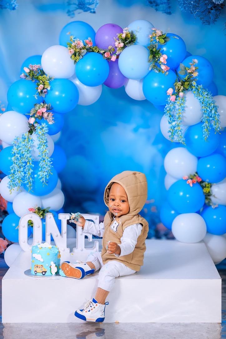 Birthday boy in a beige hoodie beside ONE letters and his cake