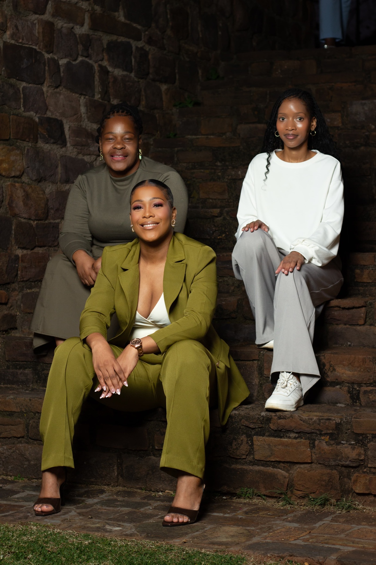 Three women in tailored outfits seated on stone steps