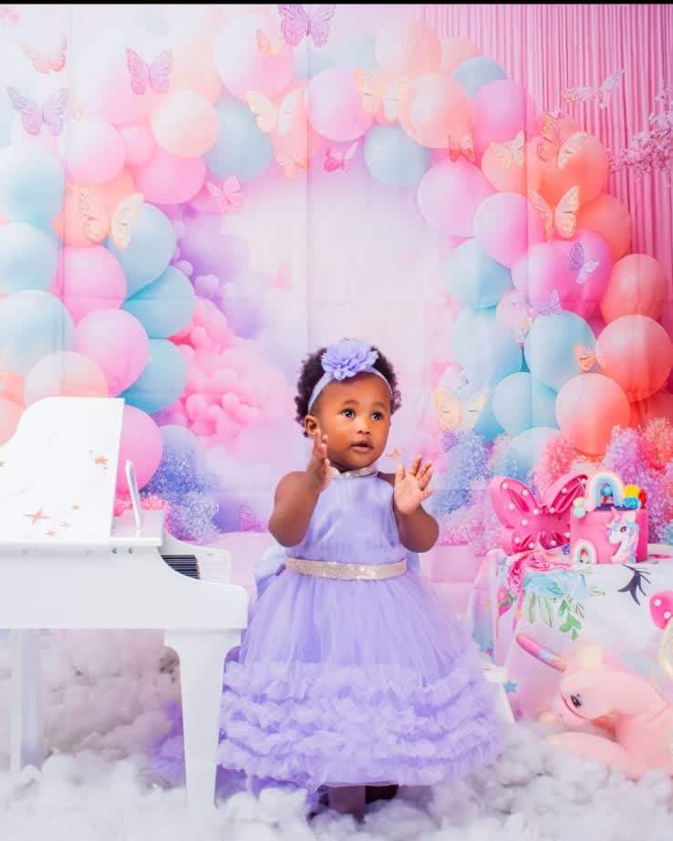 Baby girl in a lilac gown beside a white piano