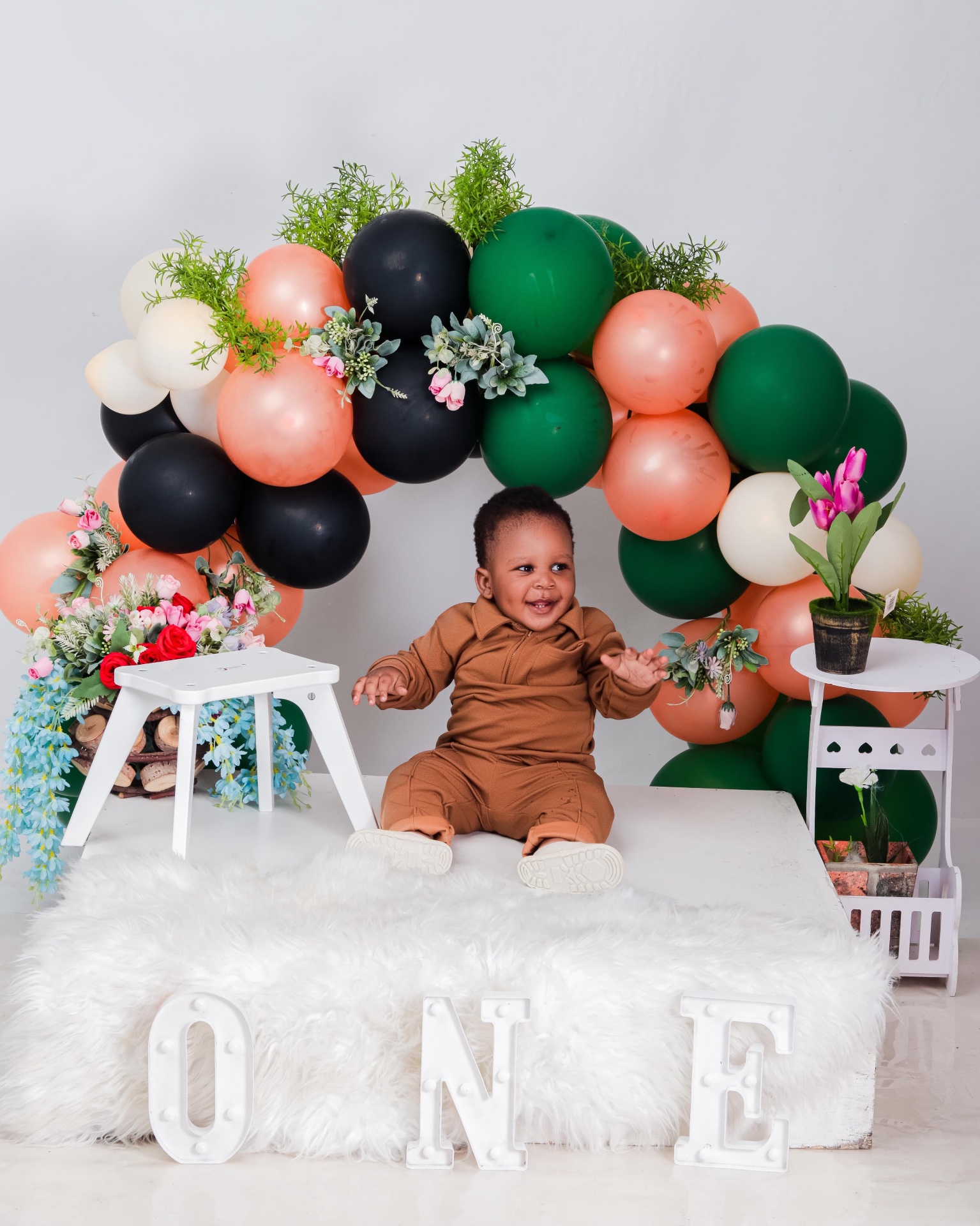 Smiling one-year-old boy in front of a floral balloon arch