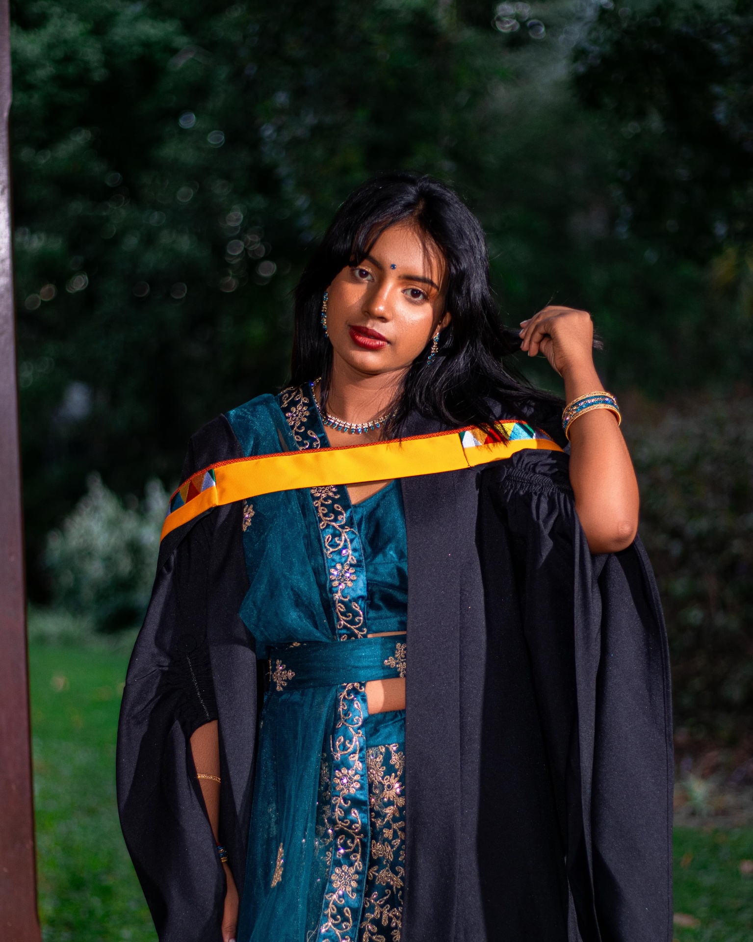 Graduate in a teal and gold outfit with gown outdoors