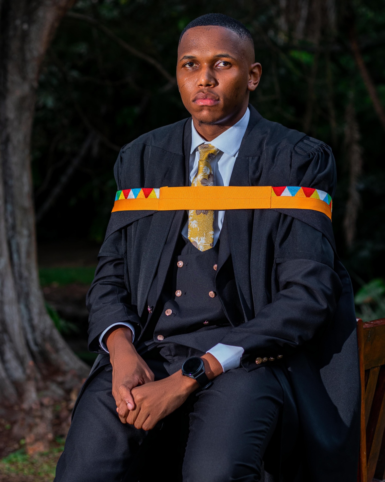 Graduate seated outdoors wearing a beaded sash