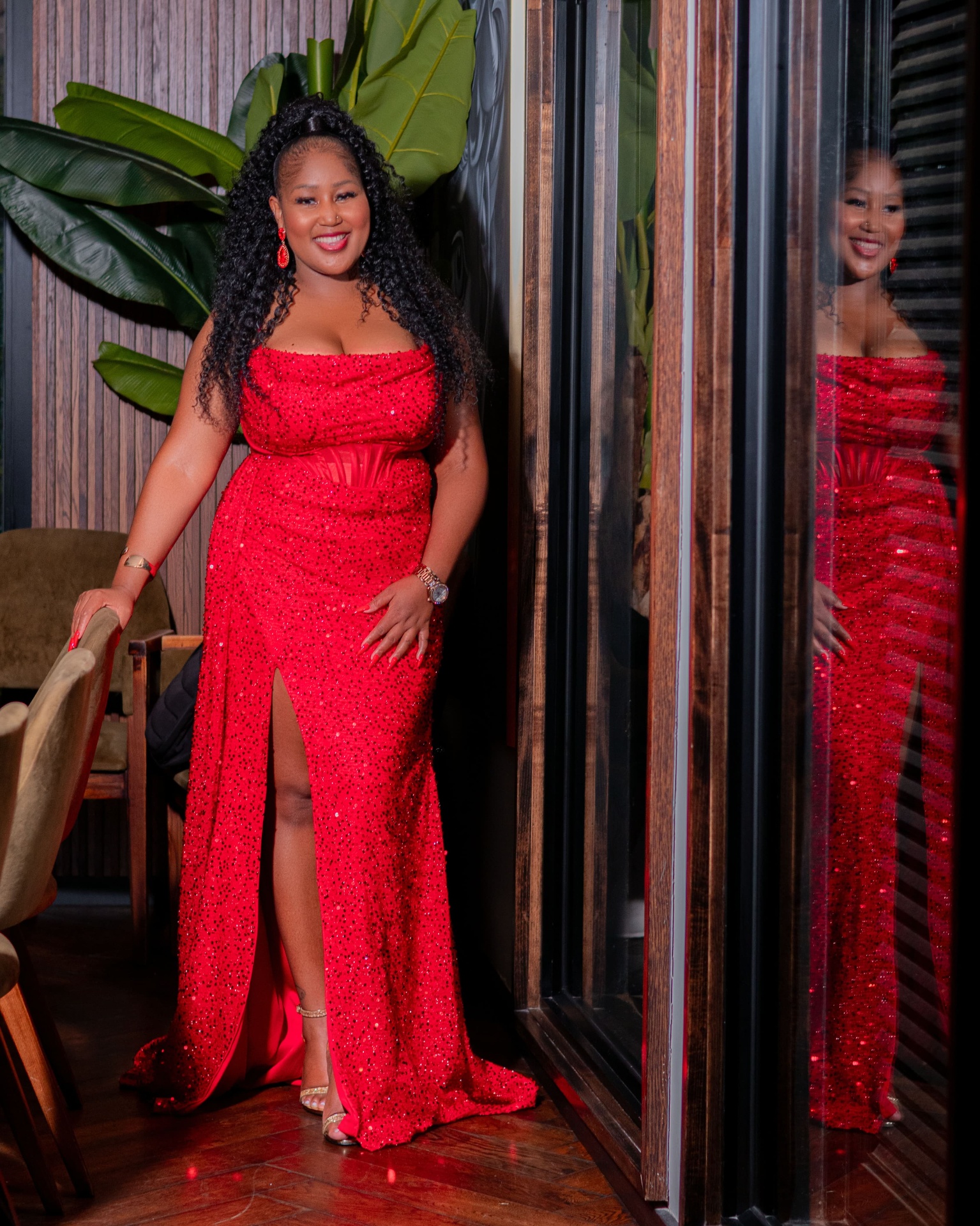 Woman in a red sequin gown standing beside a mirrored window