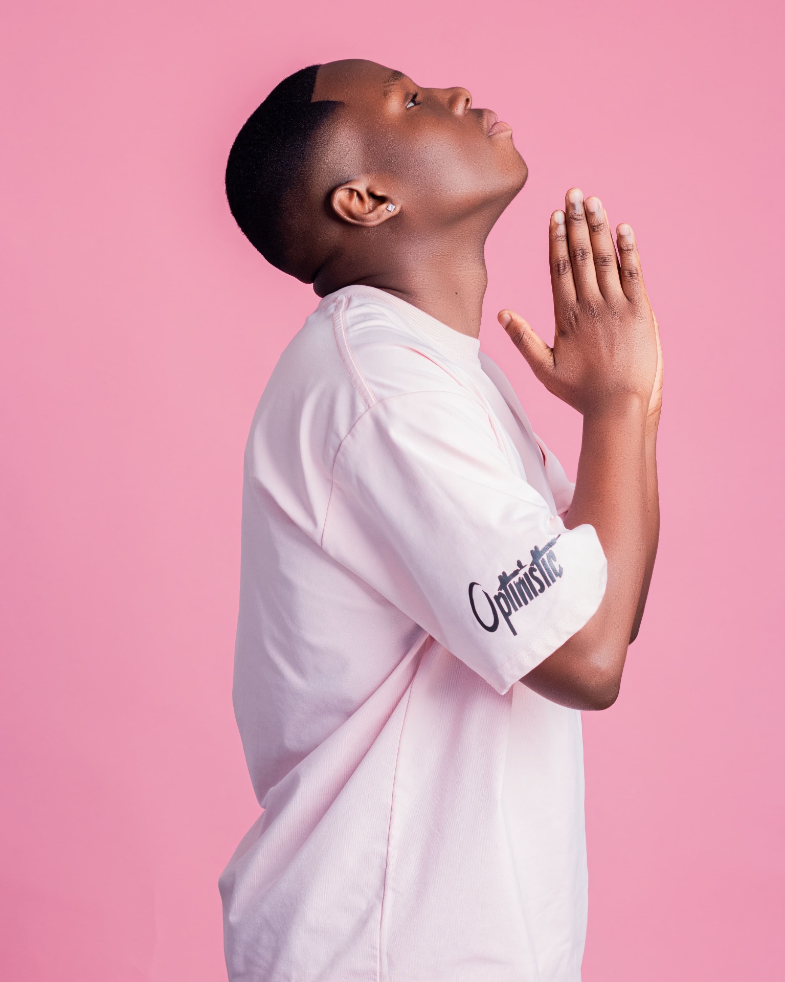 Side portrait of a man in a pale pink T-shirt with hands together