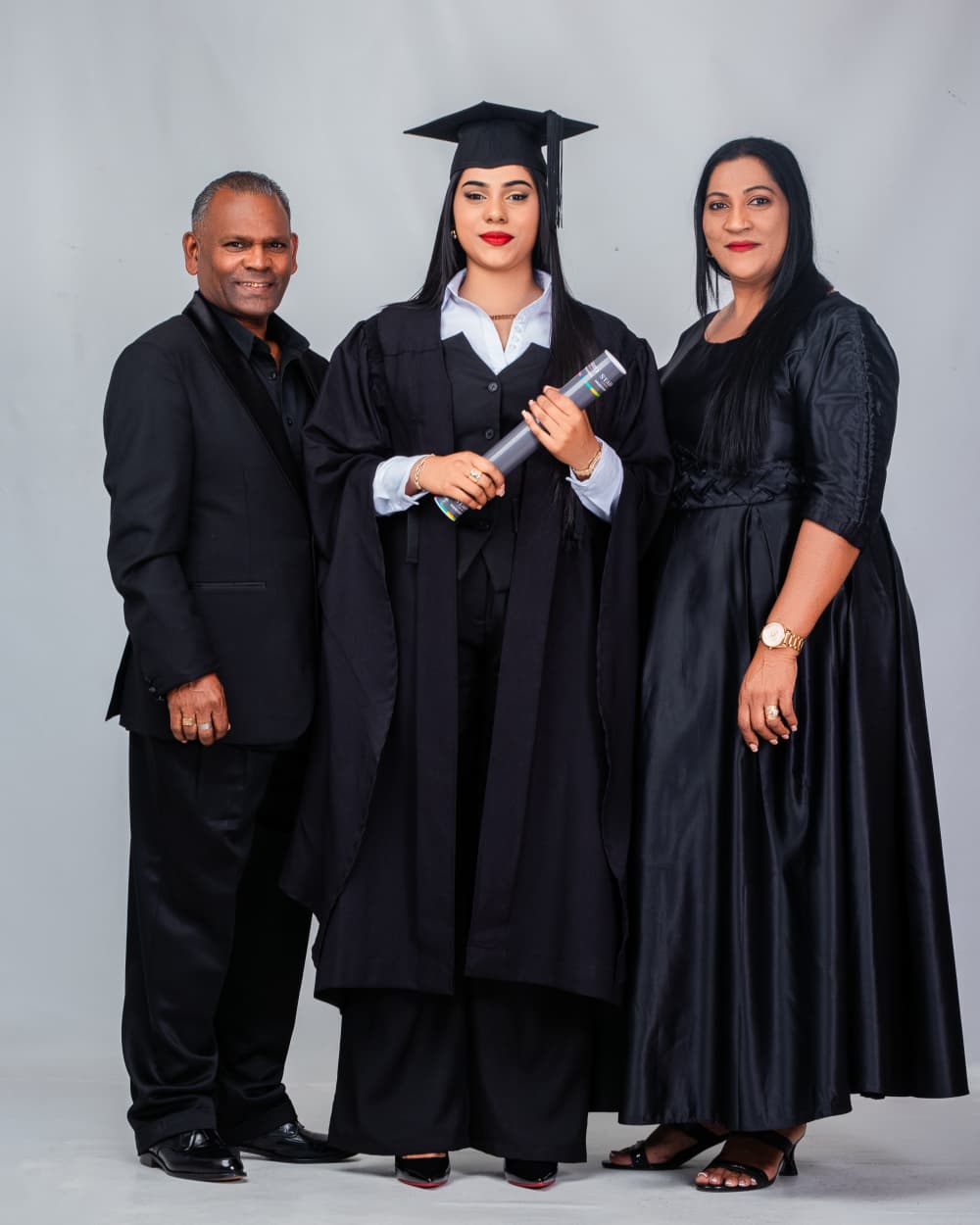 Graduate in cap and gown with her parents in studio