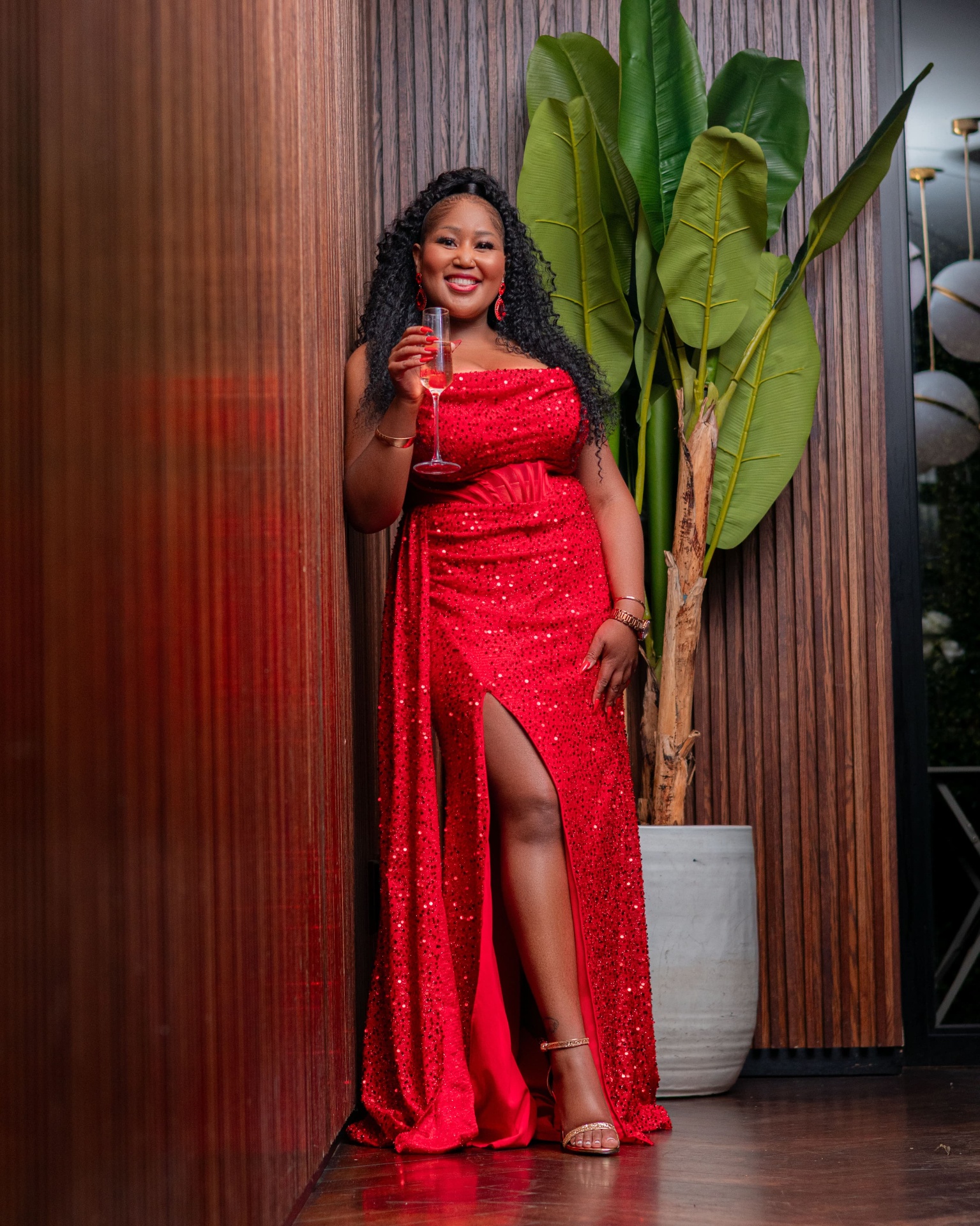Woman in a red sequin gown with champagne beside a wooden wall
