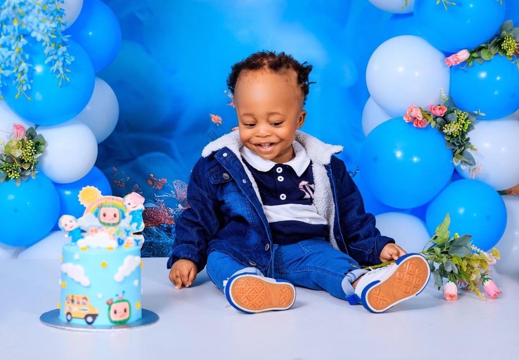Smiling baby boy in denim beside his first birthday cake